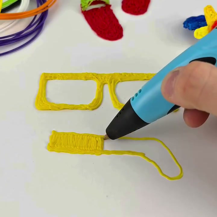 3Dペンで紙の上にメガネのフレームとつるを描く様子